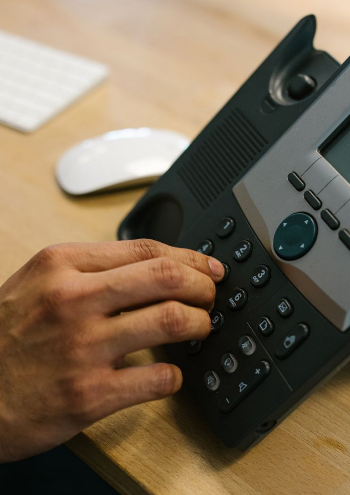 Eine Hand wählt eine Nummer an einem Telefon auf einem Schreibtisch